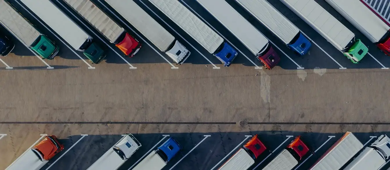 Aerial view of multiple semi-trucks parked diagonally in a lot, with colorful truck cabs lined up neatly in two rows.